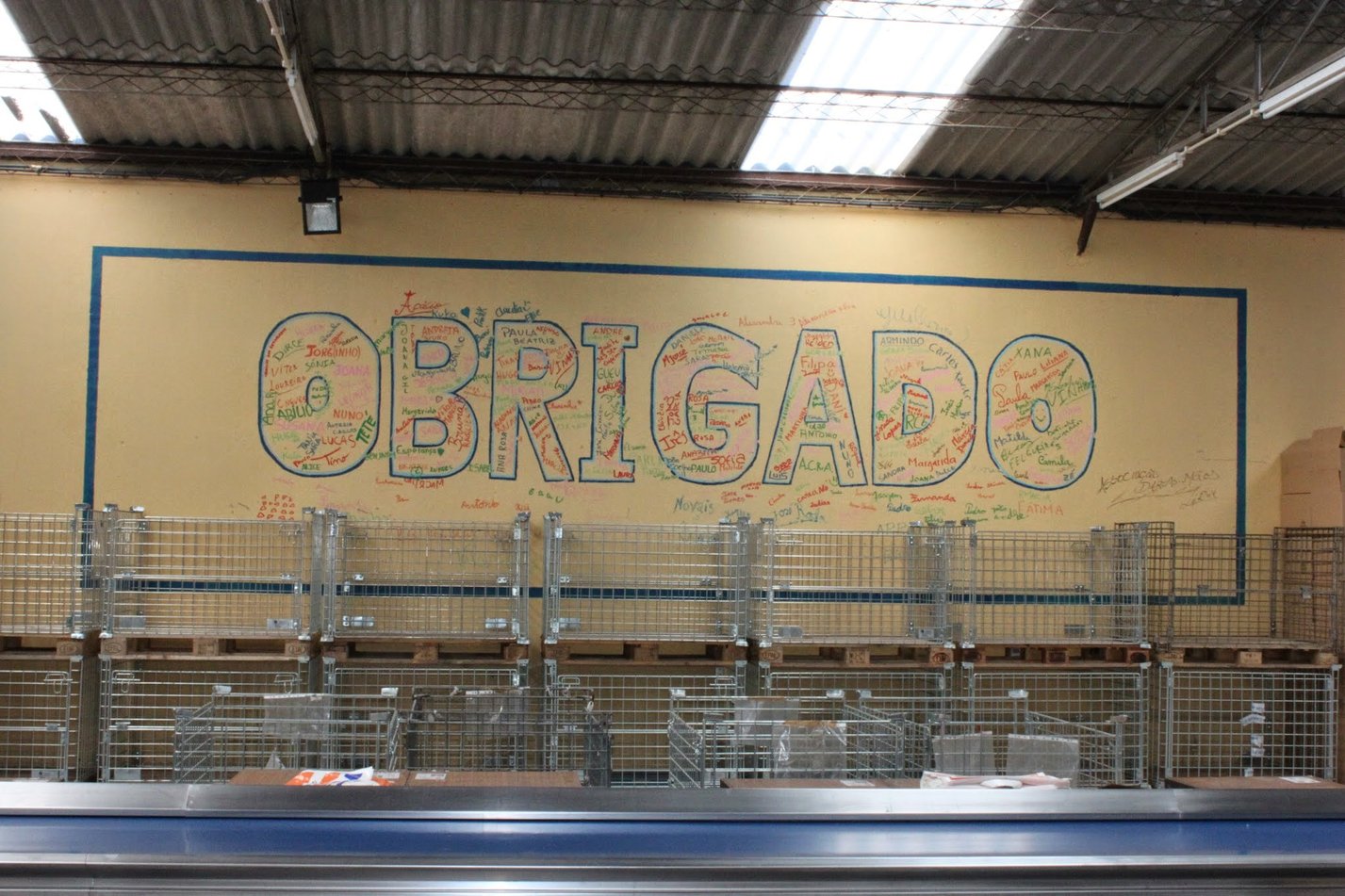 Mural com a palavra OBRIGADO no armazém, com centenas de assinaturas de voluntários ao longo dos anos